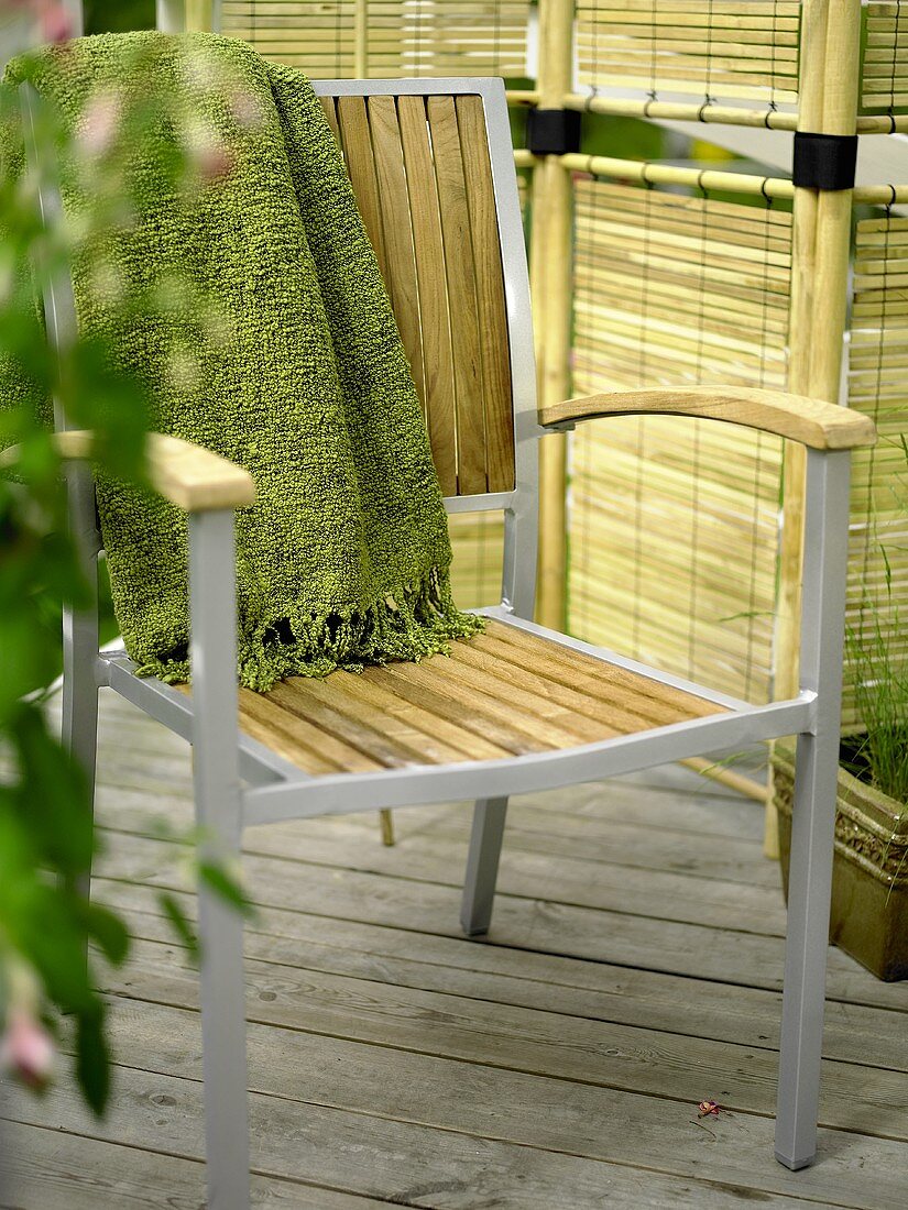 Decke auf Gartenstuhl mit Metallgestell und Holzflächen vor Rattan Paravent
