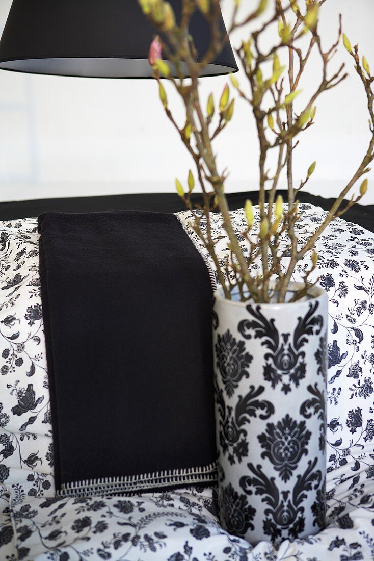 White vase with black oriental design in front of a table with a black throw blanket