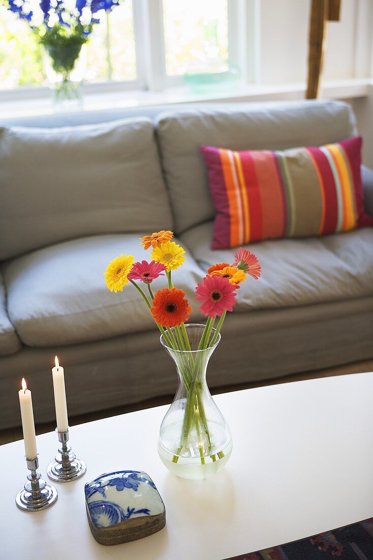 Blumen in Vase und Kerzenständer auf Couchtisch vor grauem Polstersofa mit gestreiftem Kissen