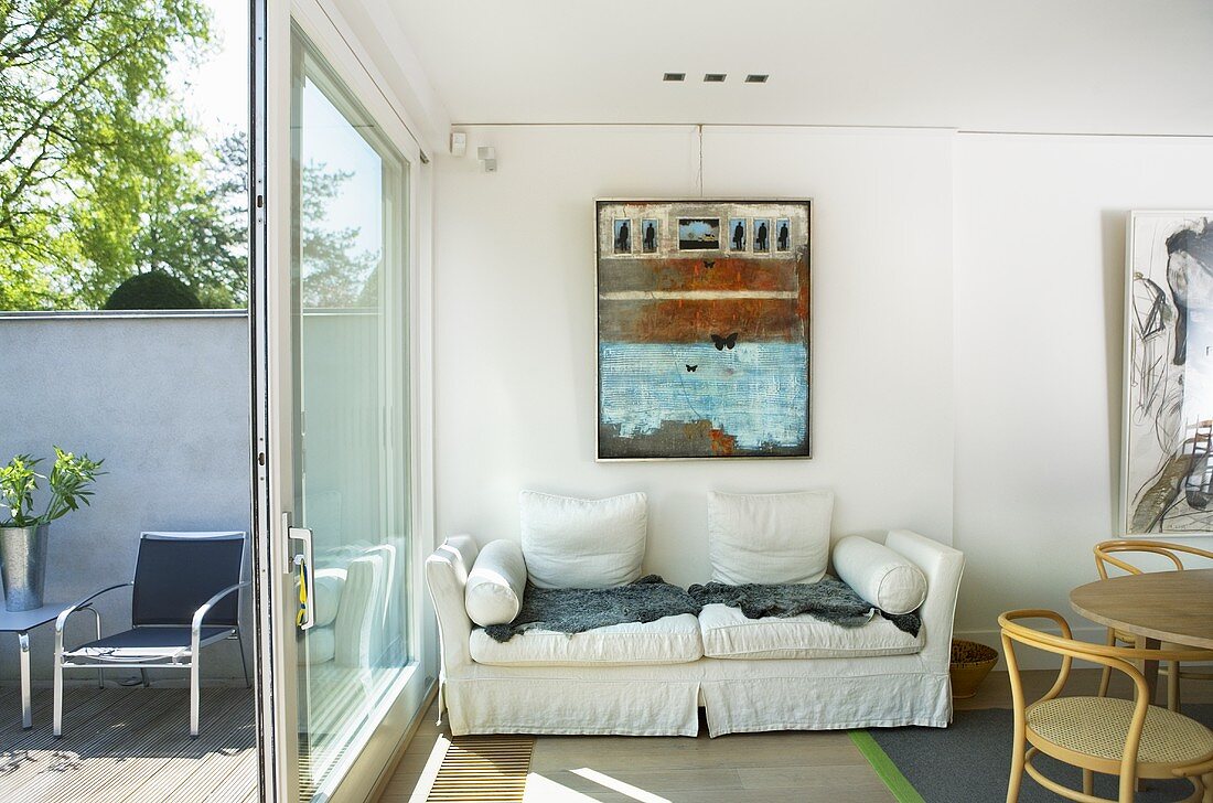 Weisses Polstersofa an Wand und Terrassenfenster mit offener Tür und Blick auf Terrasse