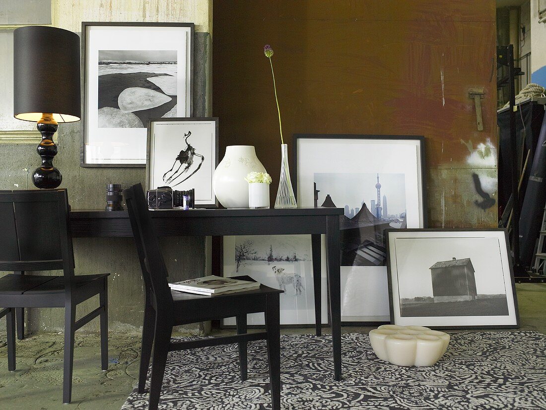 Black chairs in front of a wall tables with black table lamp and framed photos