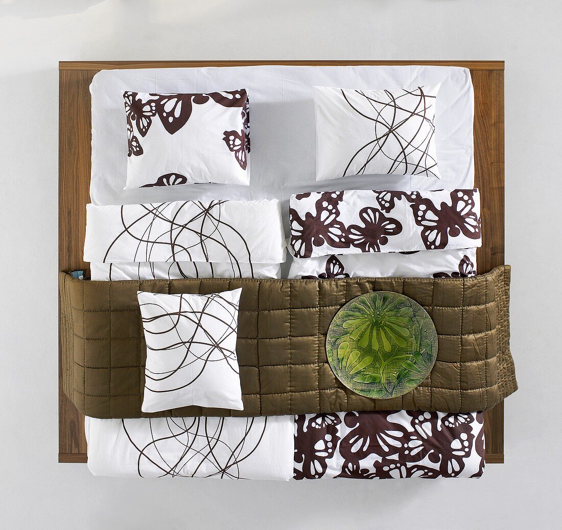 Showroom - Bett und Kissen auf Holzplatte mit gemusterter Bettwäsche und bronzefarbener Schärpe