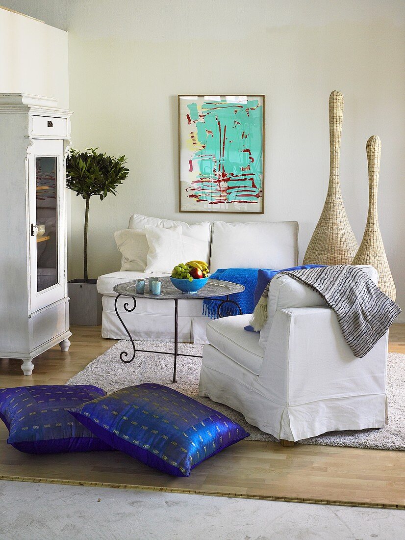 weiße Sofagarnitur mit blauen Bodenkissen und Vitrine im Landhausstil