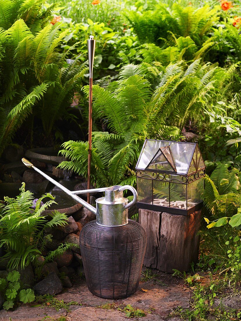 Watering can and torch next to a mini-greenhouse in the garden