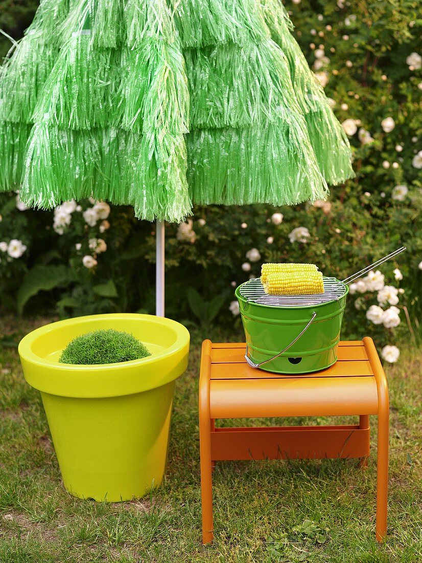 Yellow plastic plant pot and orange stool in front of green sun umbrella made from bast