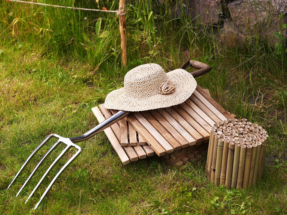 Wicker ladies hat on wooden tiles and pitchfork in the garden