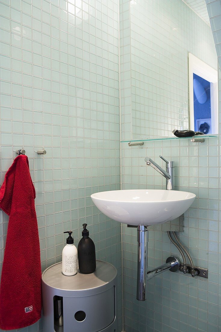 Designer wash basin with mirror in front of glass tile in a bathroom corner