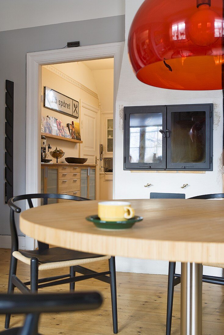 Red glass shade of a pendant lamp above a dining area and view of the kitchen through a door