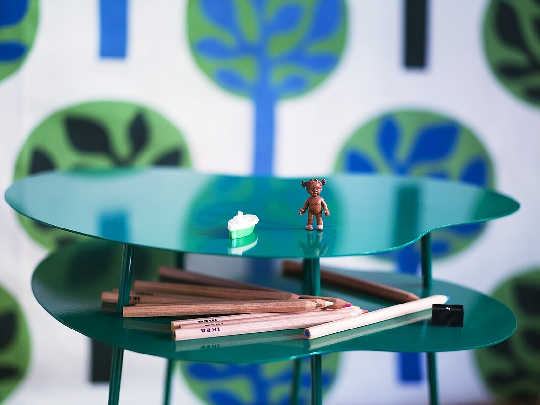 Spielzeugfigur und Buntstifte auf geschwungenem Ablagen Tisch aus grün glänzendem Metall