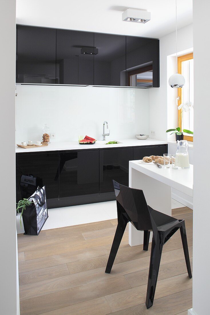 Blick in Küche mit schwarzen Hochglanzfronten, weißem schmalem Esstisch & schwarzem Kunststoffstuhl