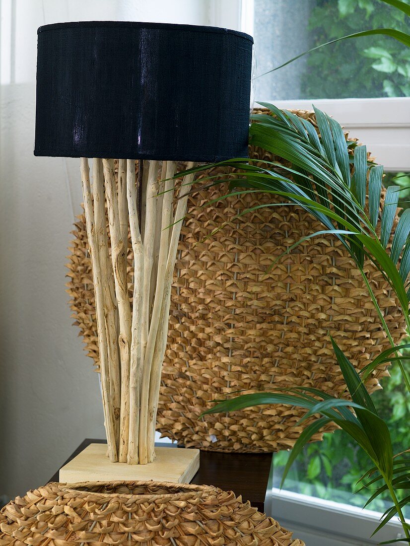 Tischlampe mit schwarzem Schirm und Fuss aus Naturholzstäben vor kugelförmigem Geflecht