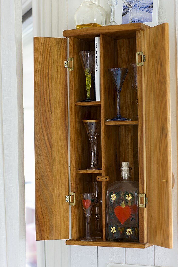 Wooden wall cupboard with open doors and view of stemware and glass bottles inside