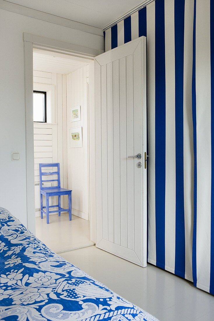 Zimmer mit blau weiss gestreiftem Vorhang und offener Zimmertür mit Blick in Vorraum