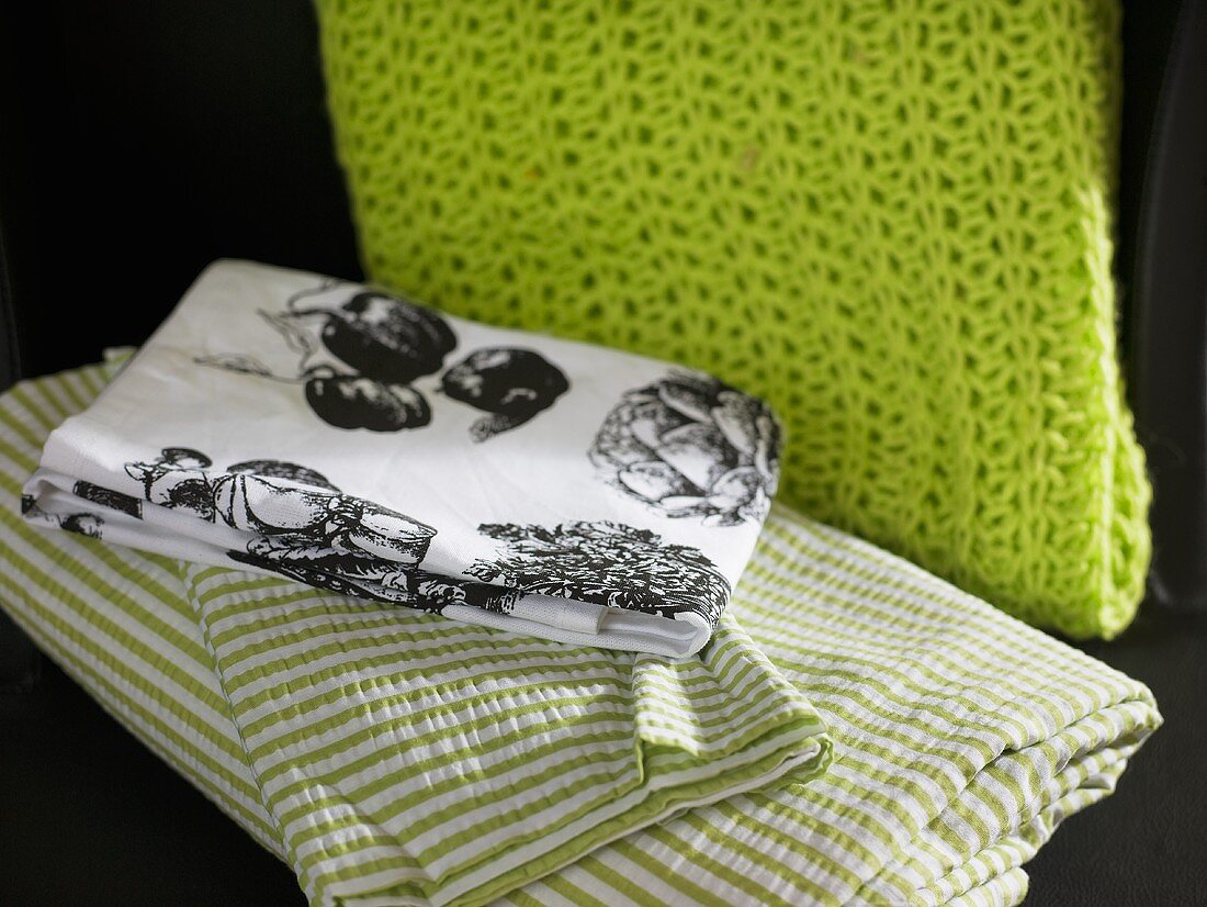 Tischdecke mit ländlichen Motiven und gestreifte Bettwäsche neben grünem Strickschal