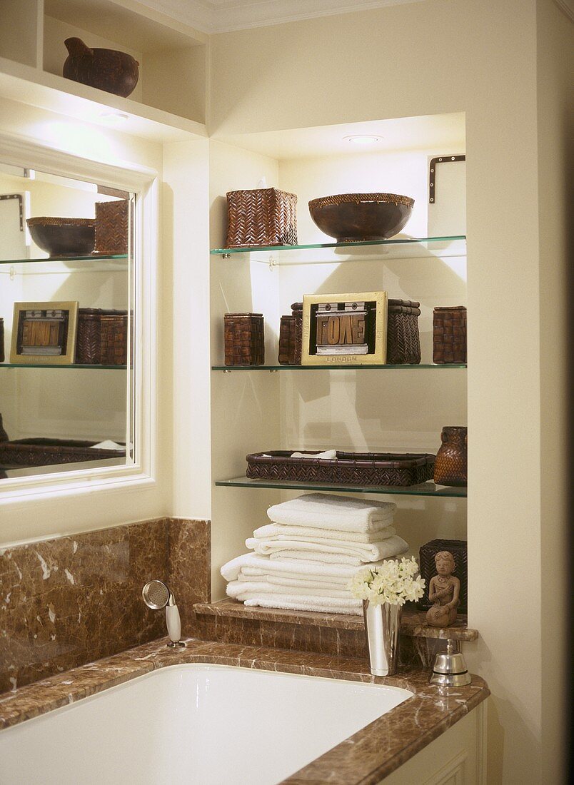 A detail of a traditional bathroom, showing a fitted bath with marble surround, glass shelves in recess