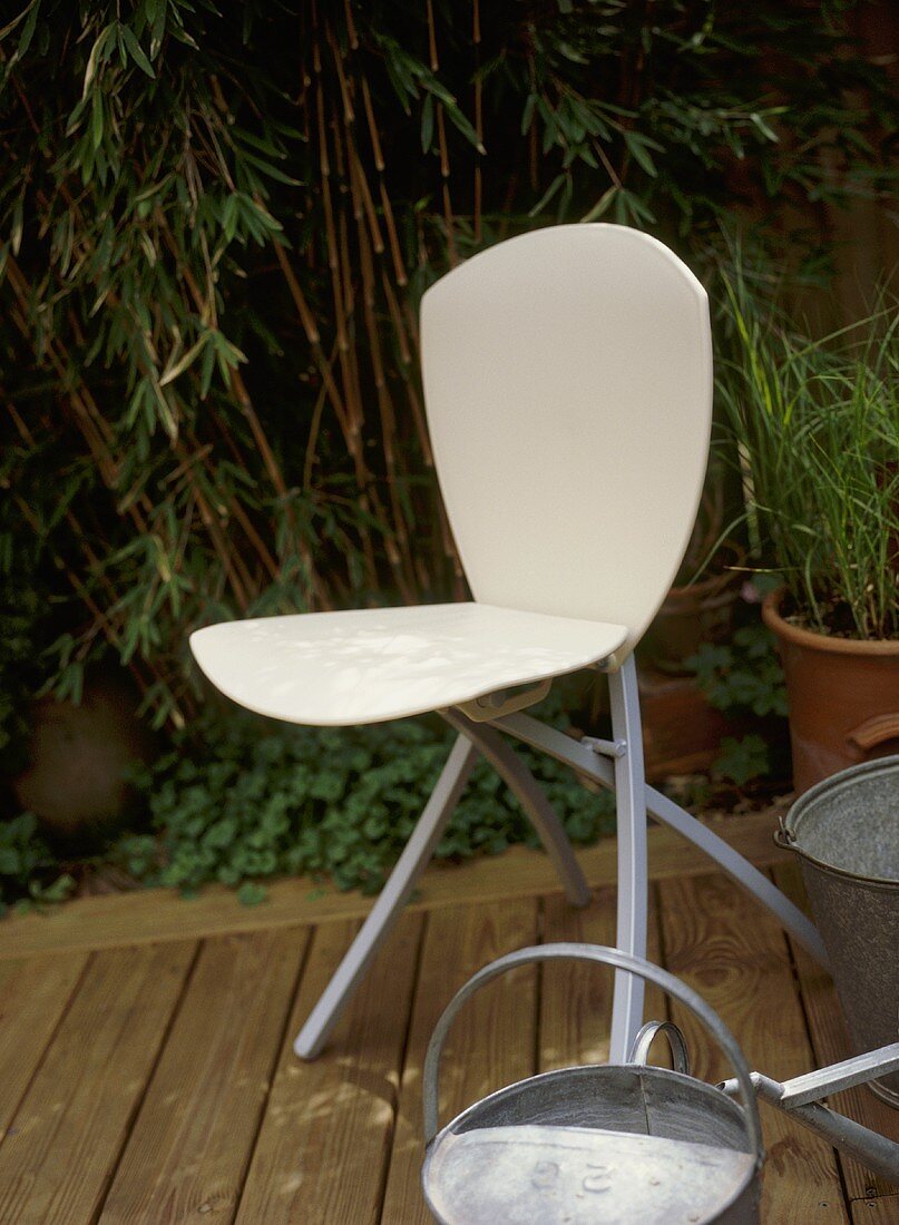 A detail of a garden showing a modern chair on a decked area, watering can