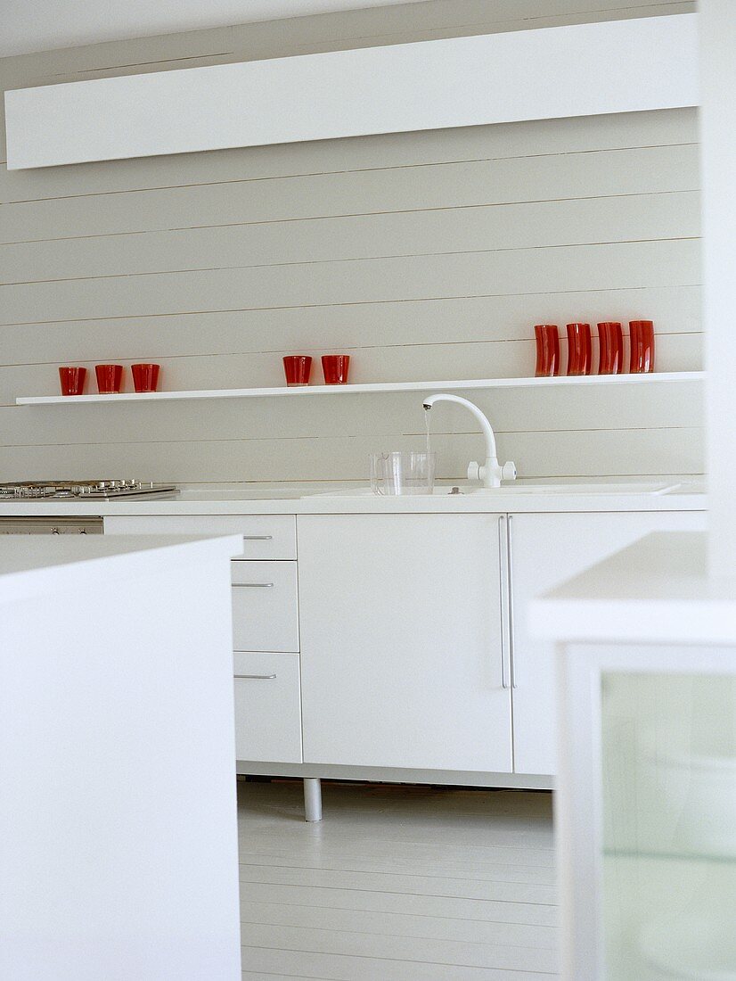 Moderne Küche mit weissen Unterschränken und roten Gläsern auf Regalablage