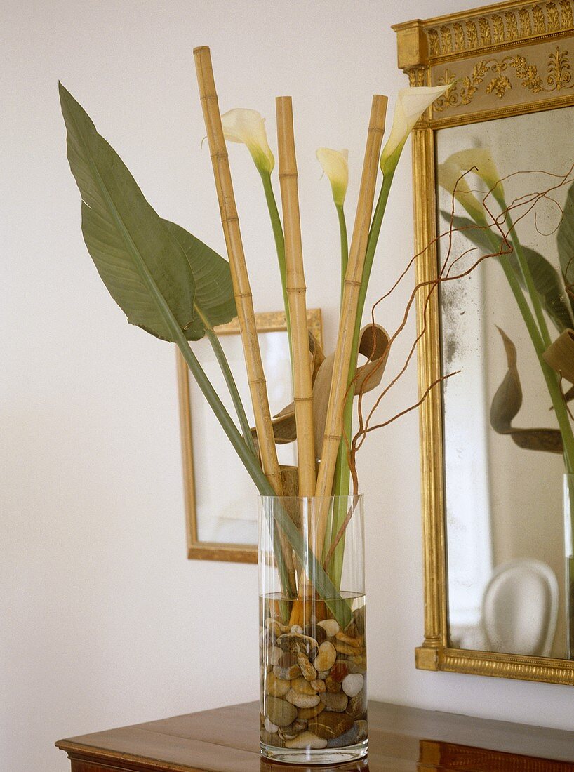 Blumenblatt, Bambusstäbe und weiße Callas in Vase vor Spiegel mit Goldrahmen