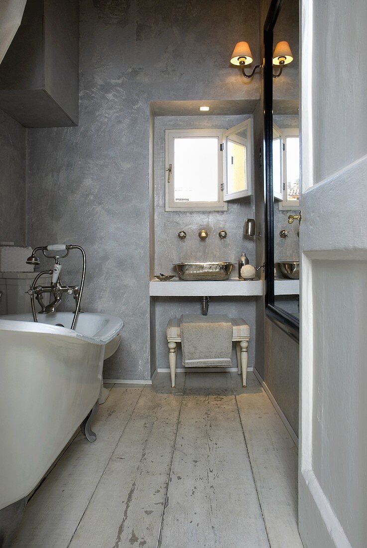 A rustic bathroom with grey walls and a washstand in the window niche