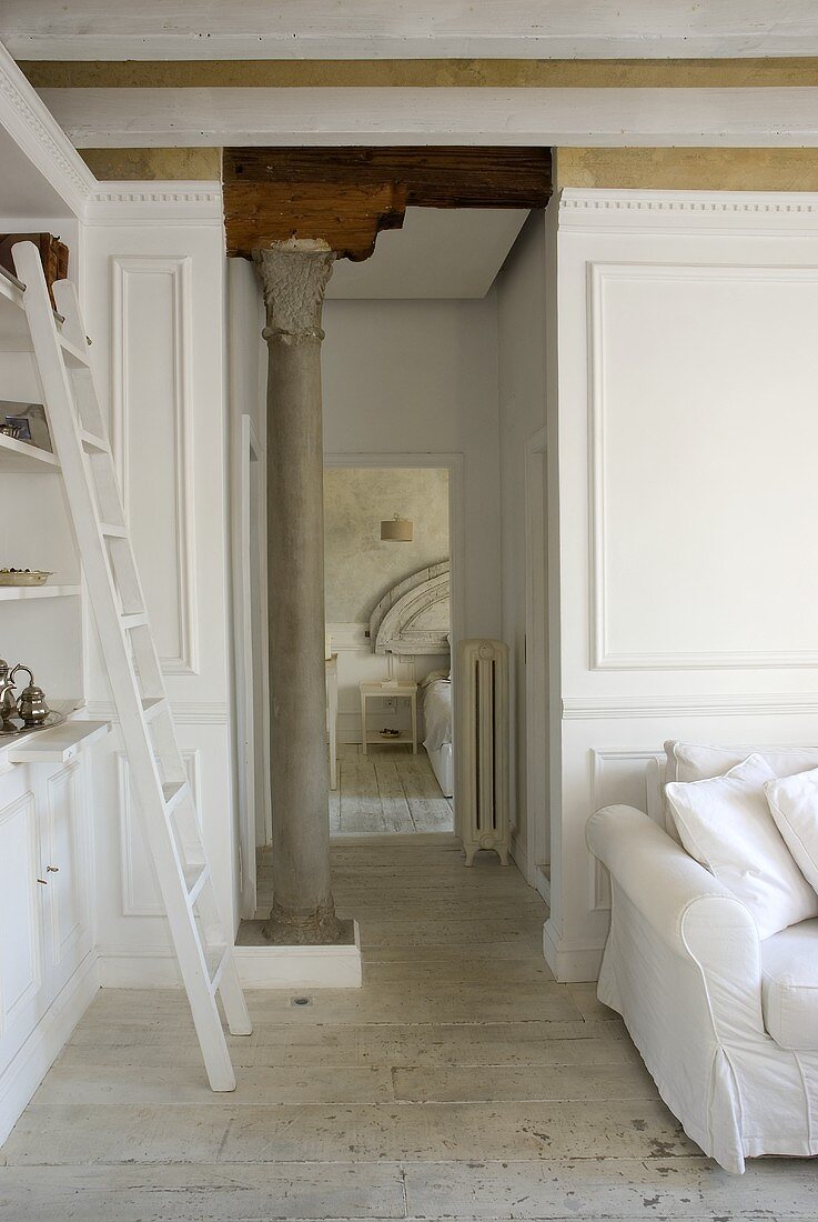 Offener Wohnraum mit weisser Leiter am Schrank und antik griechischer Säule im Flur mit offener Schlafzimmertür