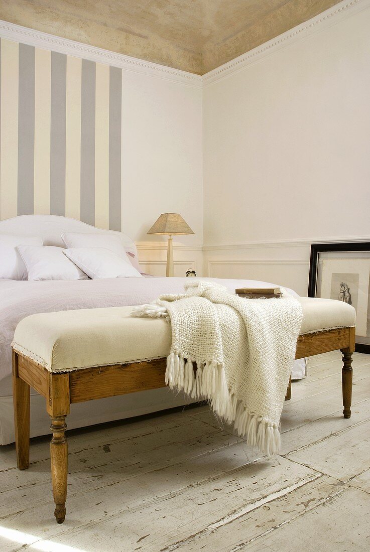 Antike Bettbank mit hellem Polster und Strickplaid vor Bett