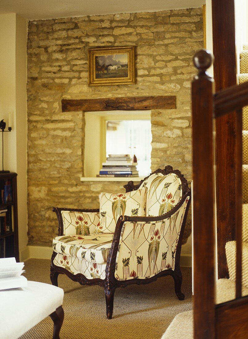 Sessel mit gemustertem Stoff vor Natursteinwand mit Fenster