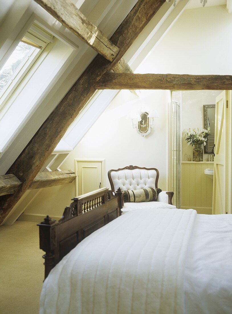 Schlafzimmer im Dachgeschoss mit Doppelbett und antikem Sessel unter rustikalem Dachstuhl