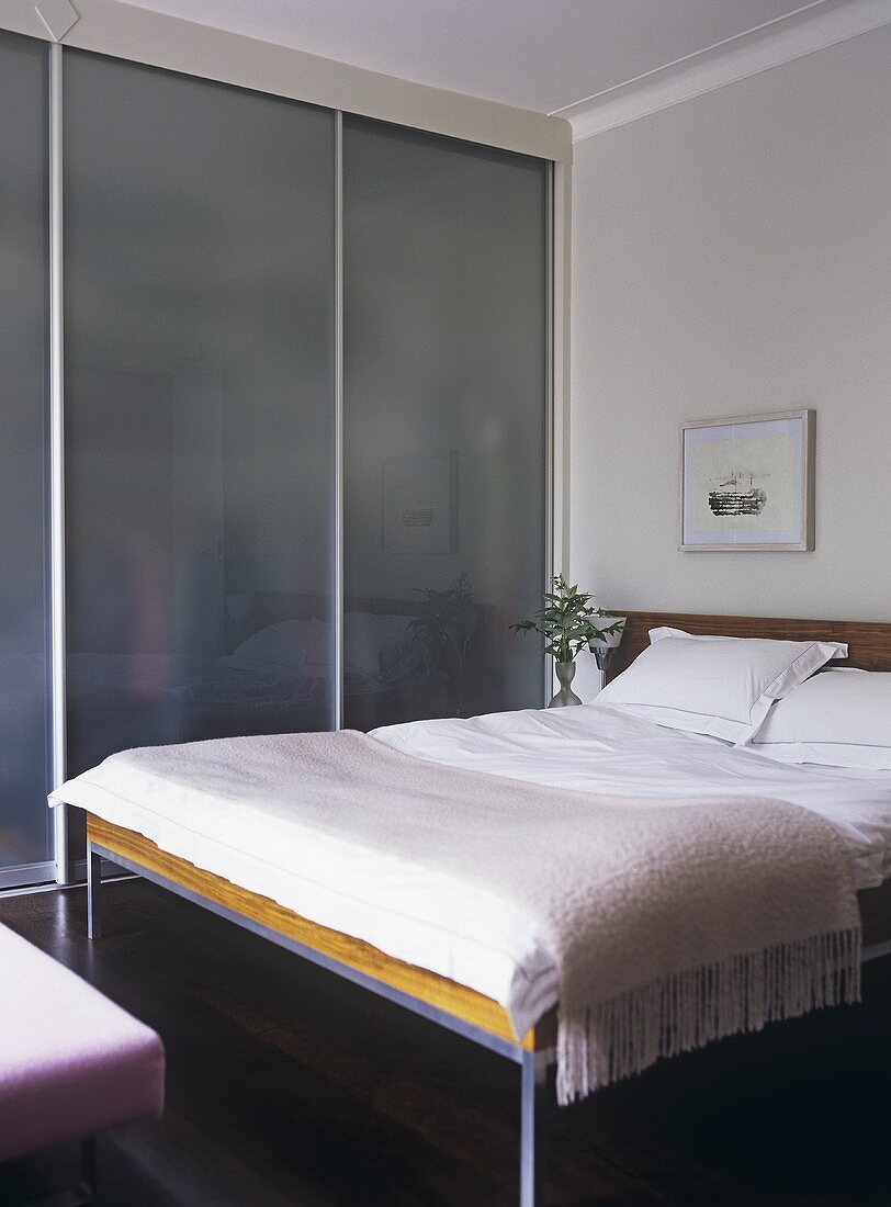 A modern, minimalist bedroom decorated in neutral colour, double bed, fitted wardrobe with sliding door,