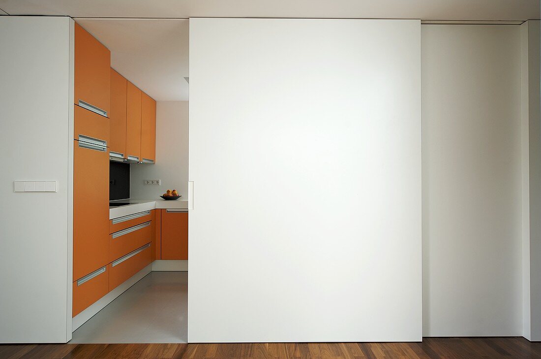 A modern kitchen with orange units and half open white sliding doors