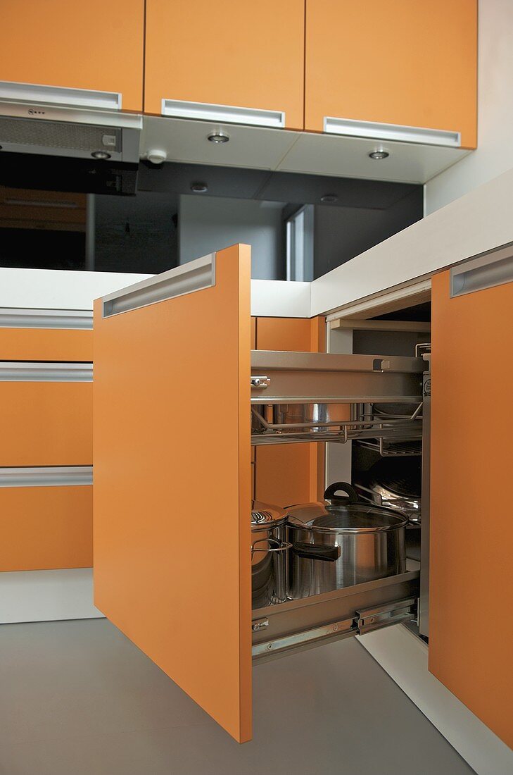 Offener Küchenunterschrank mit orangefarbener Front und Edelstahltöpfen
