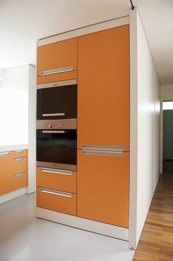 Moderne offene Küche mit orangefarbenen Fronten am Einbauschrank mit Einbaugeräten