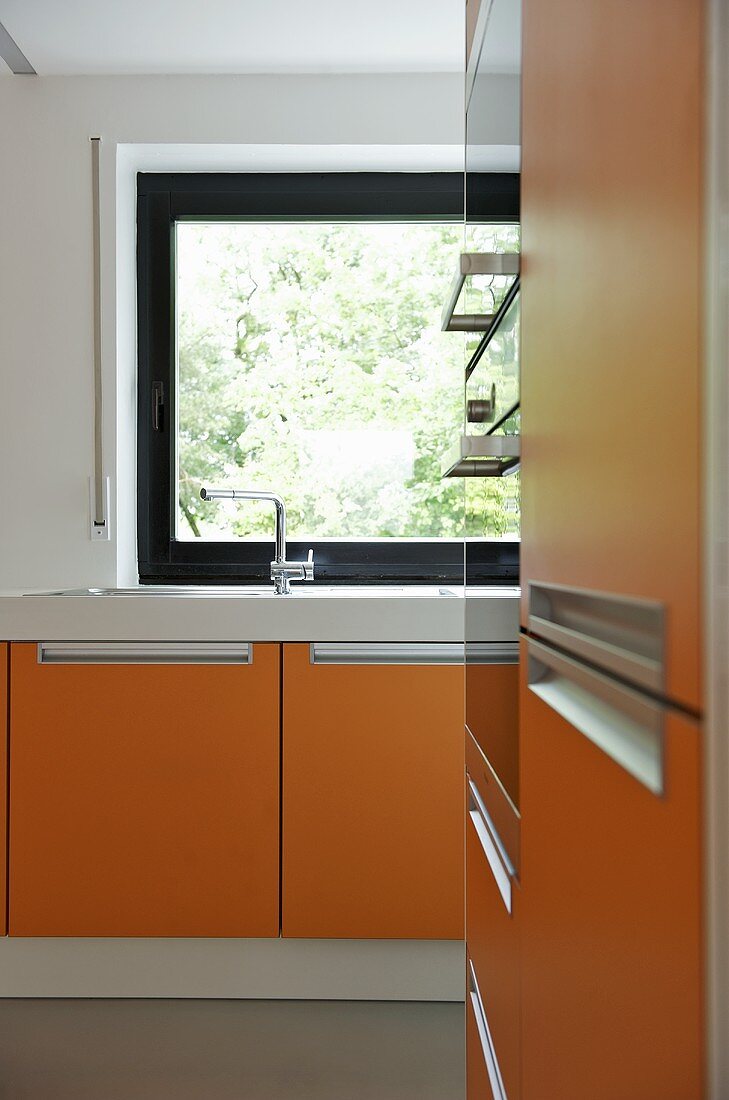 Moderne Küche mit orangefarbenen Fronten und Fenster mit dunklem Rahmen