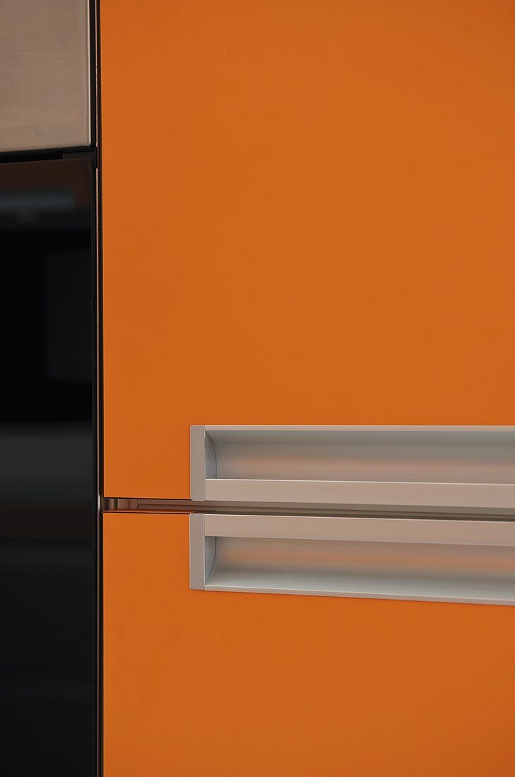 Küchenschrank mit orangefarbener Front und eingelassener Griffmulde