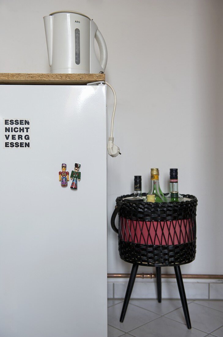 Wasserkocher auf Kühlschrank und Korb mit Flaschen auf Hocker