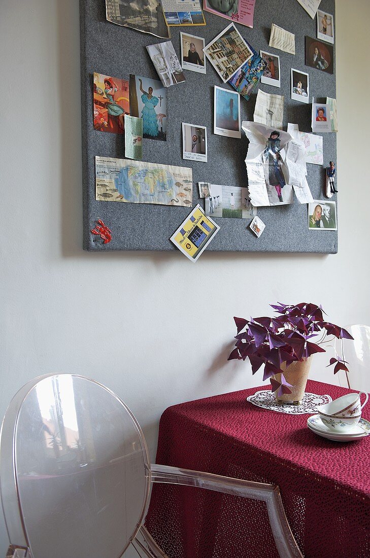 Transparenter Kunststoffstuhl neben Tisch mit roter Tischdecke und Wandboard mit Photos