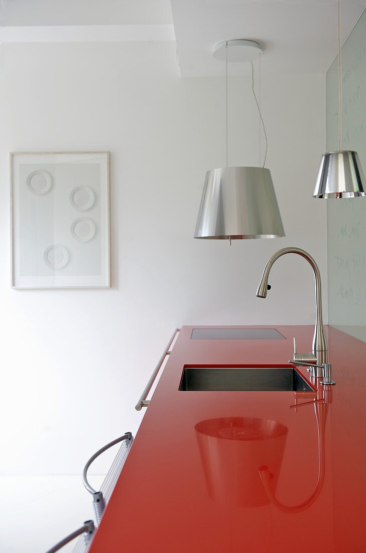Spüle und Armatur in roter Arbeitsplatte aus Kunststoff und Hängeleuchten mit Metallschirm