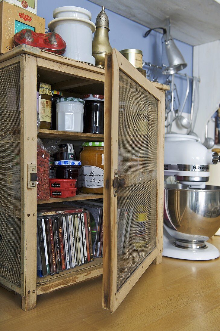 Jars of jam and cds in wooden cabinet on worktop