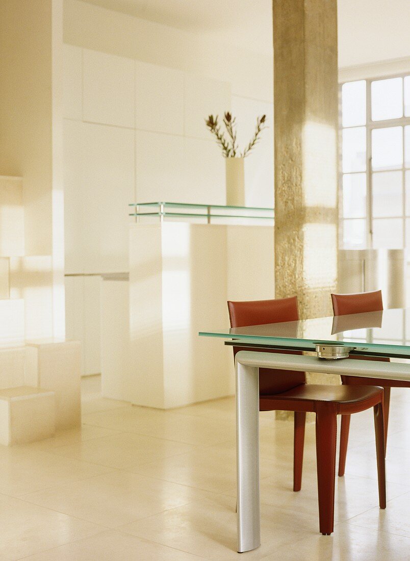 Esstisch mit Glasplatte und roten gepolsterten Stühlen in offener Küche