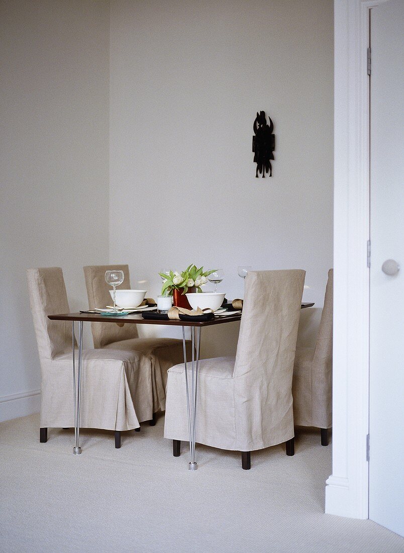 Linen covered chairs at table set for dinner in neutral colour dining room