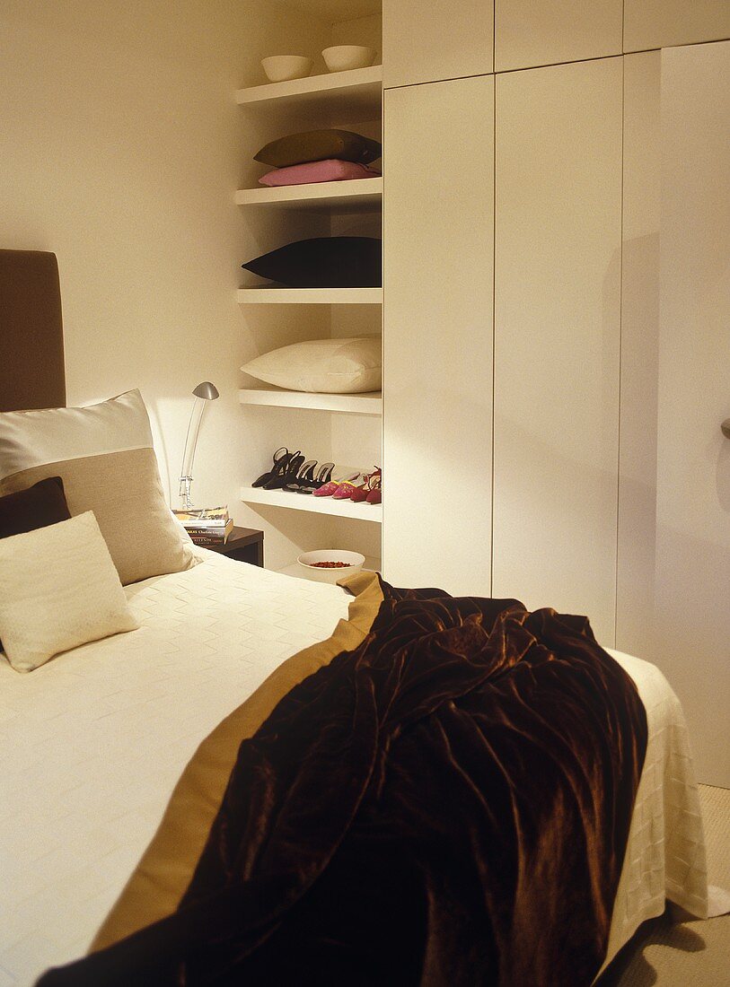 Doppelbett mit glänzender brauner Tagesdecke und weißem Einbauschrank mit Regal