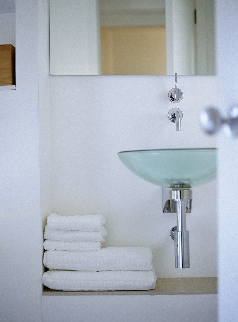 Bathroom with designer glass wash basin and folded towels on ledge.