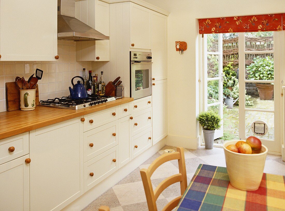 Küche mit weißen Schrankfronten und kugelförmigen Holzgriffen und Gartentür