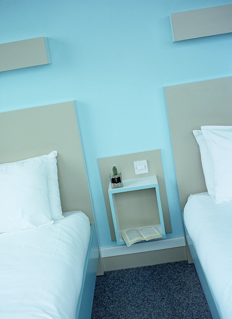Zwei Einzelbetten mit grauem Kopfteil vor blauer Wand