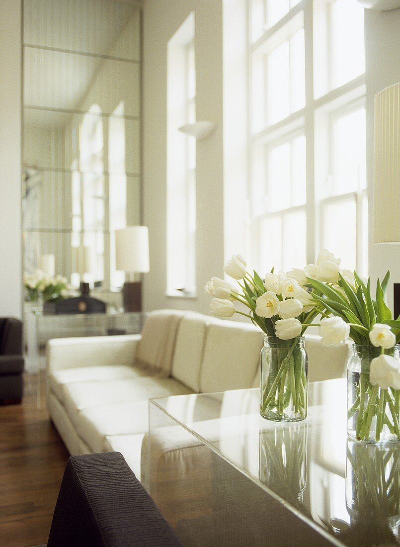 Vasen mit weißen Tulpen auf durchsichtigem Kunststofftisch neben Sofa