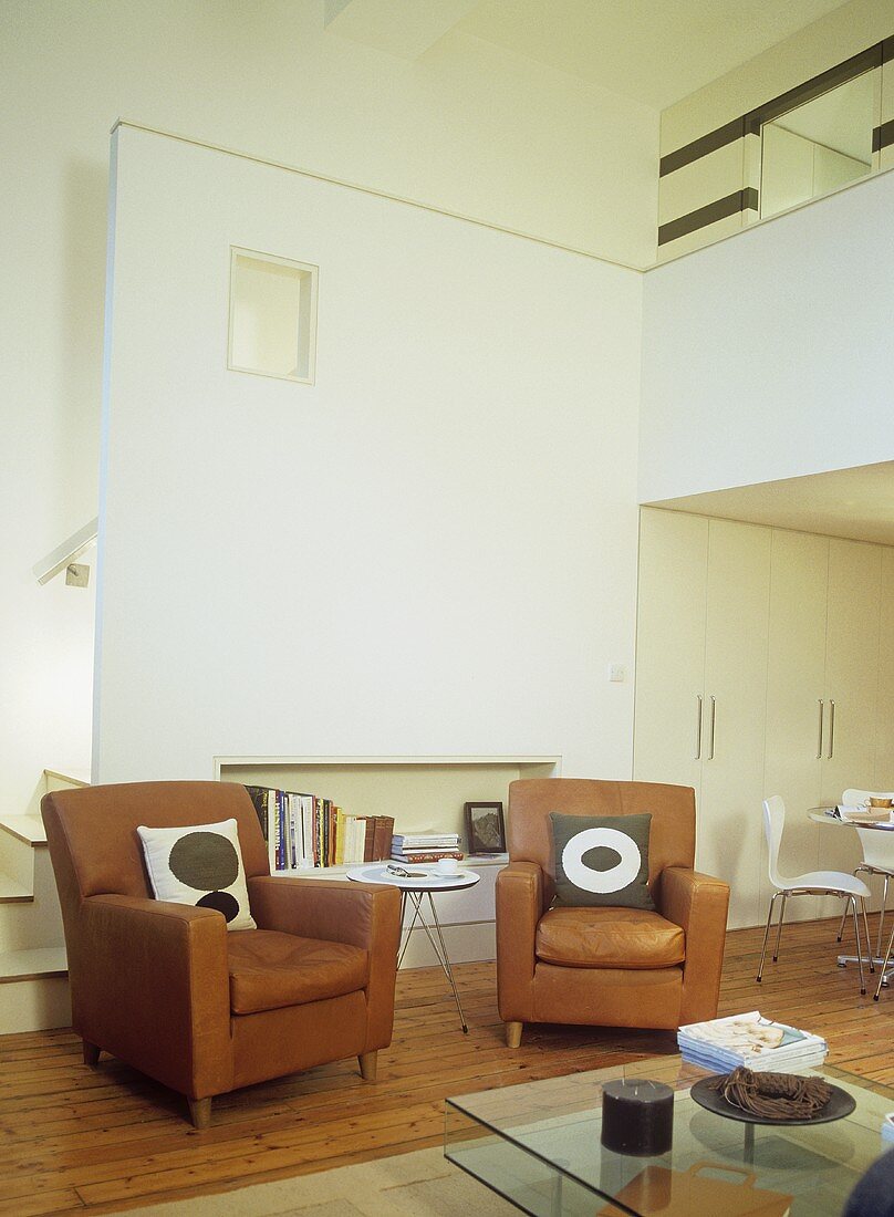 Zwei braune Polstersessel mit Couchtisch aus Glas im offenen Wohnraum
