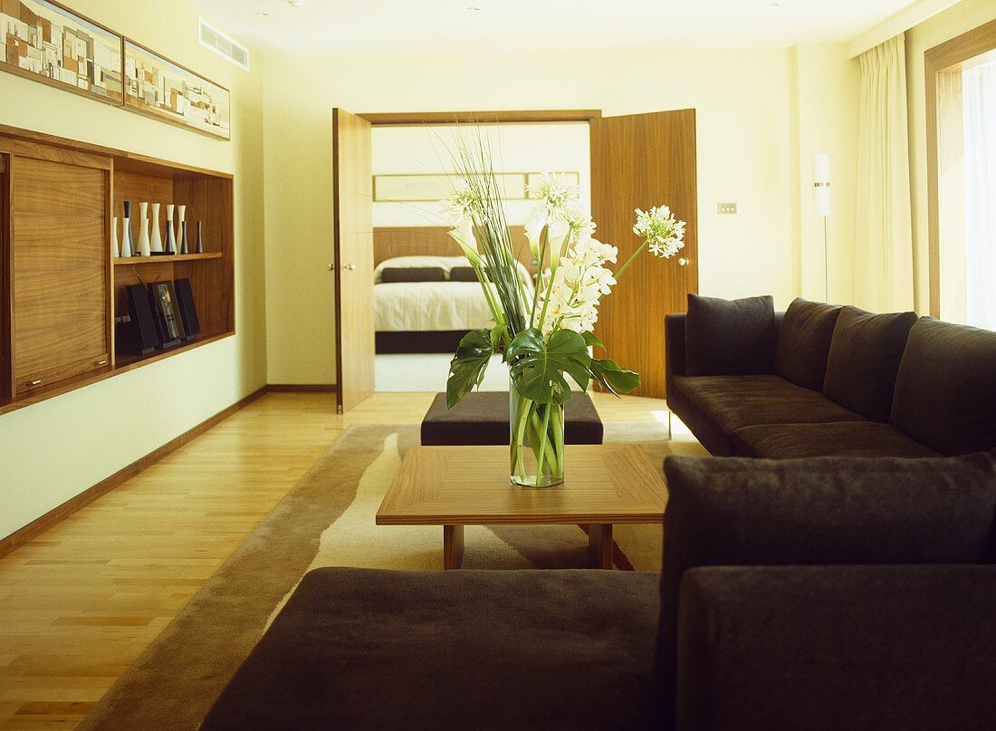 Braunes Sofa übereck und Couchtisch aus Holz mit offener Flügeltür und Blick ins Schlafzimmer