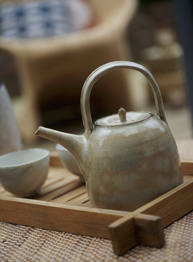 A detail of ceramic teapot and beakers on wooden tray,