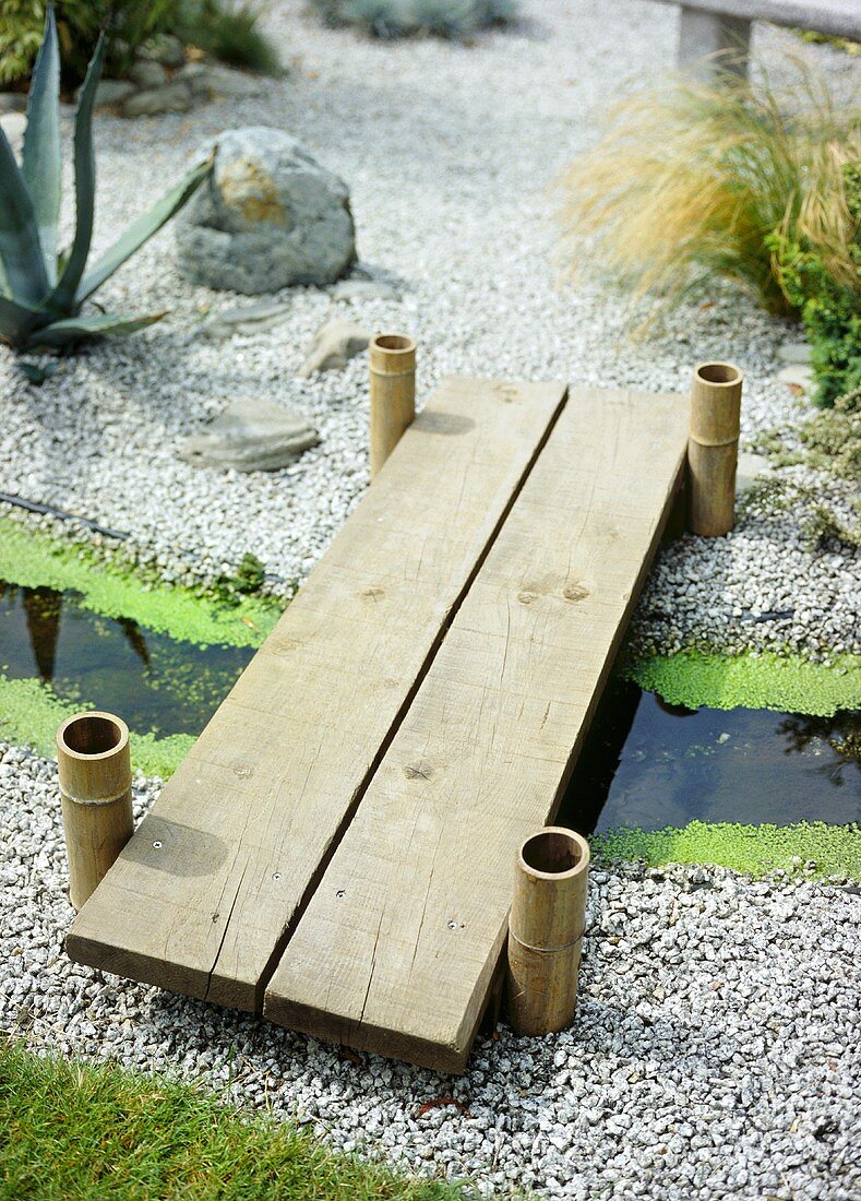 A garden detail, Japanese style dry gravel, wooden foot bridge over a small stream, bamboo posts,