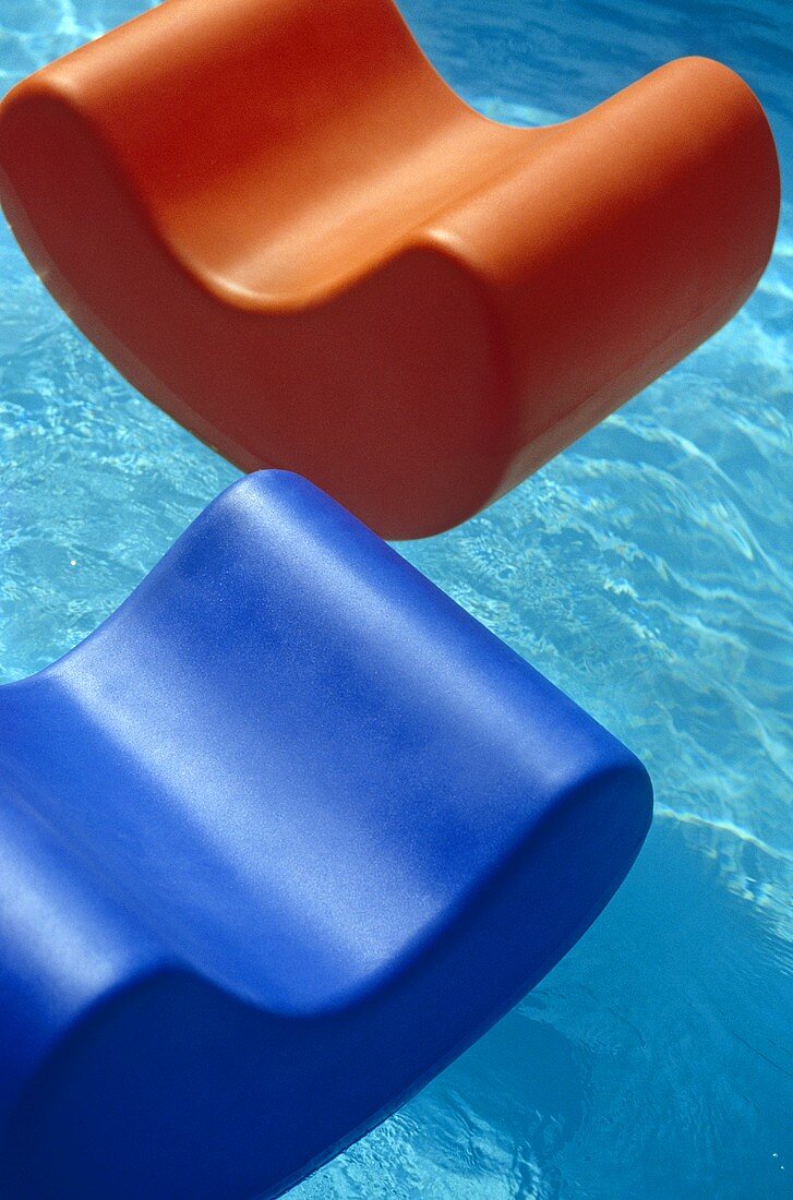 Oranger und blauer Kunststoffsessel schwimmen im Pool