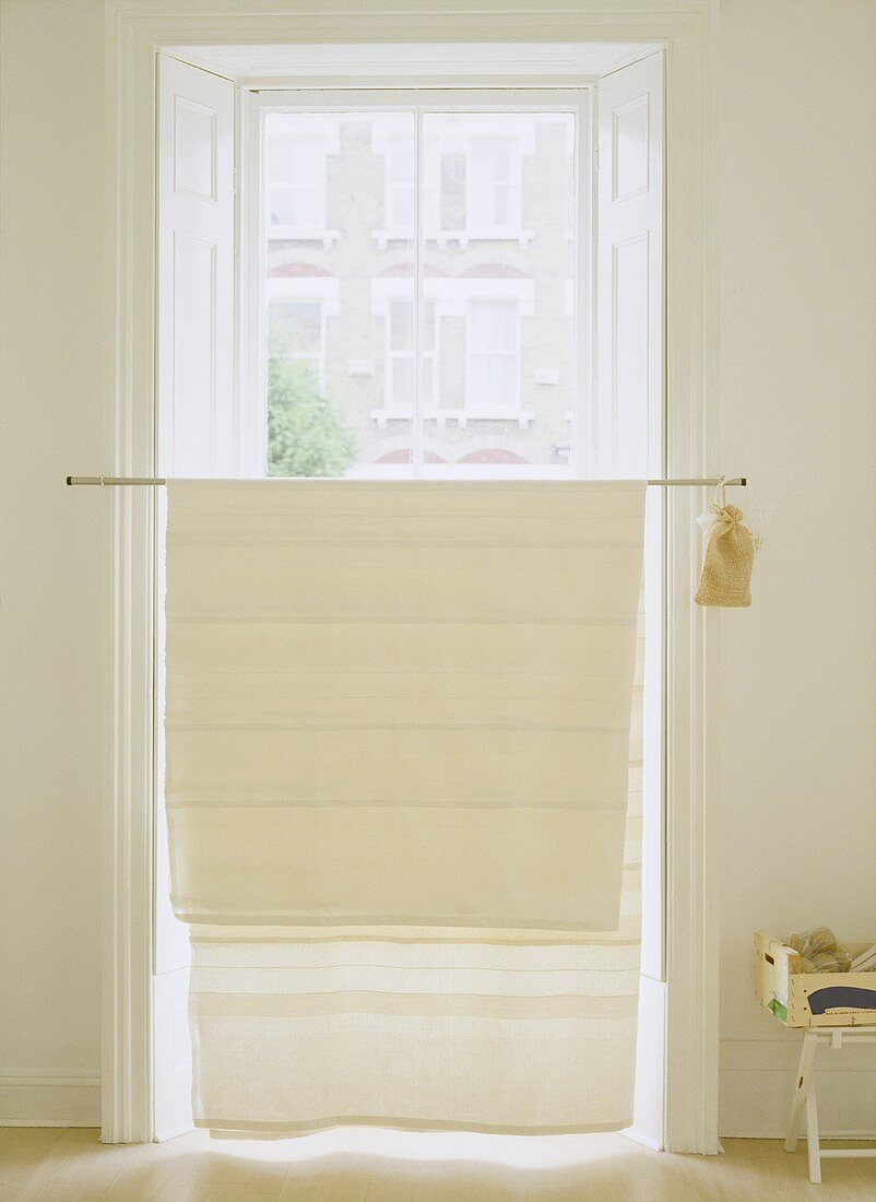 A detail of a simple window with a neutral curtain draped over pole and used as a blind